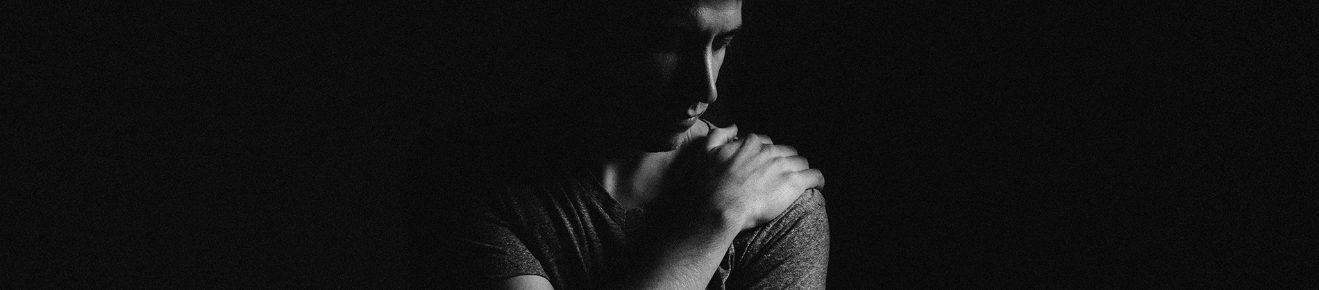 A black and white photo of a man looking down with his hand on his shoulder A black and white photo of a man looking down with his hand on his shoulder