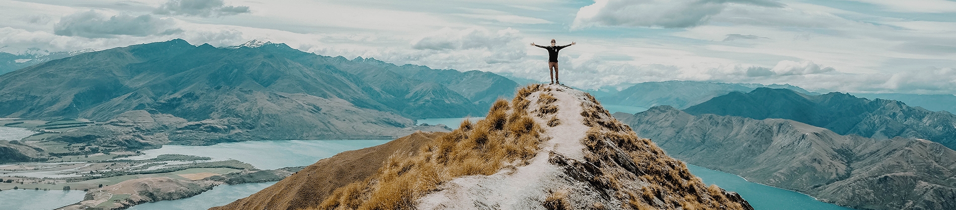 A man stood on top of a grassy cliff with his arms out wide A man stood on top of a grassy cliff with his arms out wide