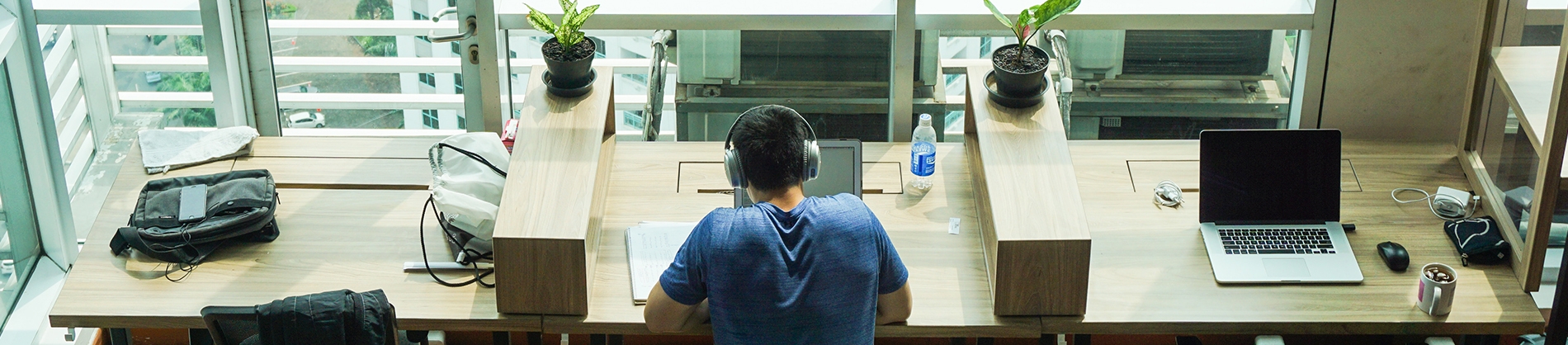 A man sat at a wooden desk with headphones on working A man sat at a wooden desk with headphones on working