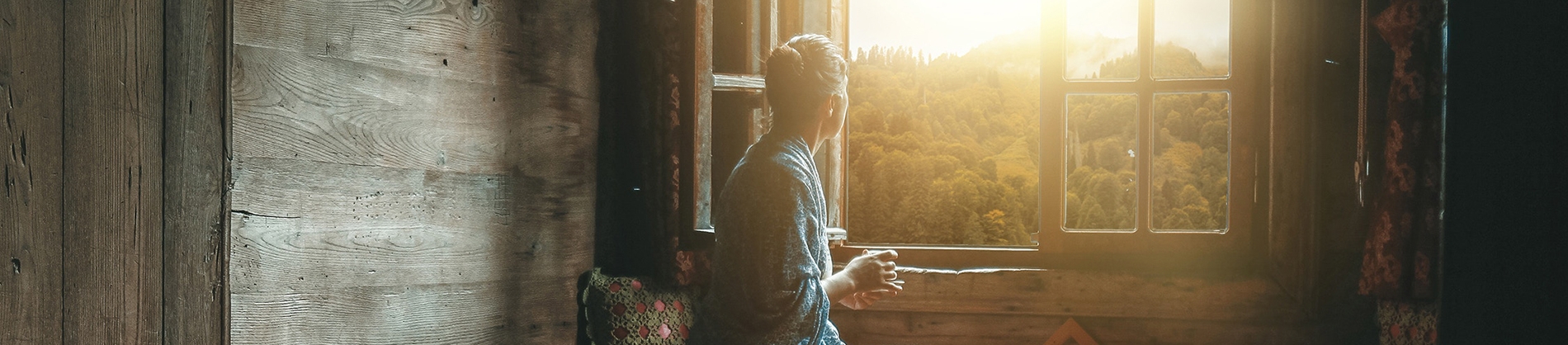 A women sat looking out of a wooden cabin window A women sat looking out of a wooden cabin window