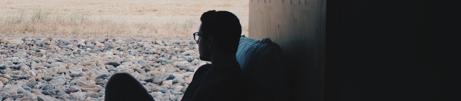 A man leaning against a wooden wall looking out over pebbles A man leaning against a wooden wall looking out over pebbles