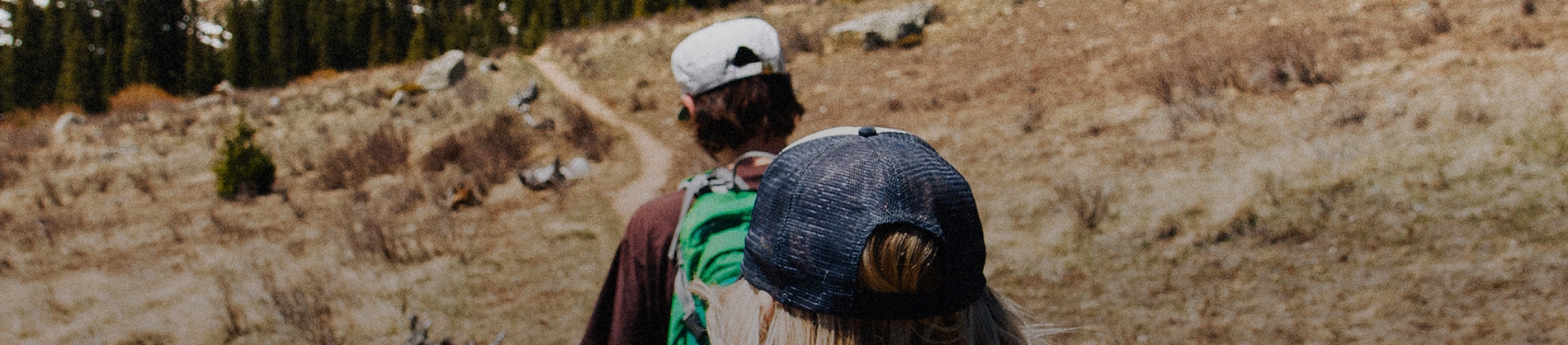 Two people trekking down a path towards a forest Two people trekking down a path towards a forest