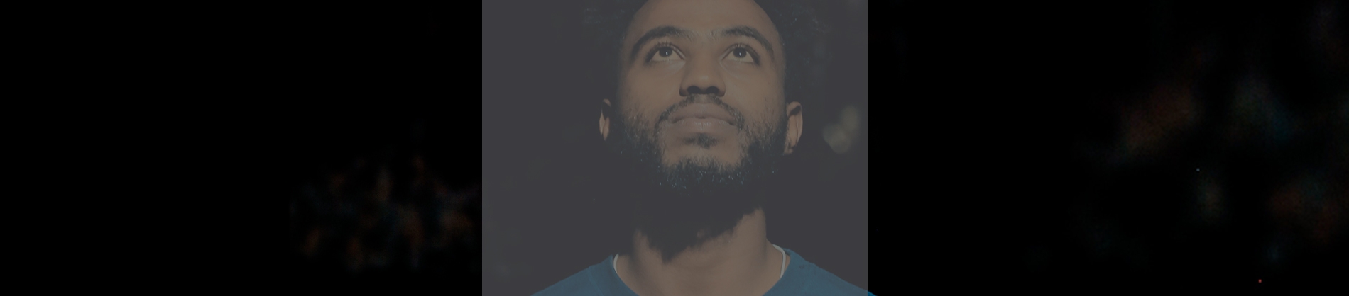 A man with a dark background looking up with light shining on his face A man with a dark background looking up with light shining on his face