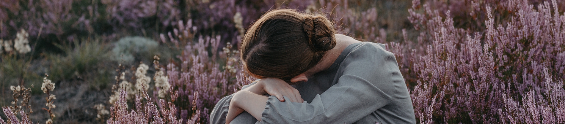 A woman sat in a field with her head on her knees A woman sat in a field with her head on her knees