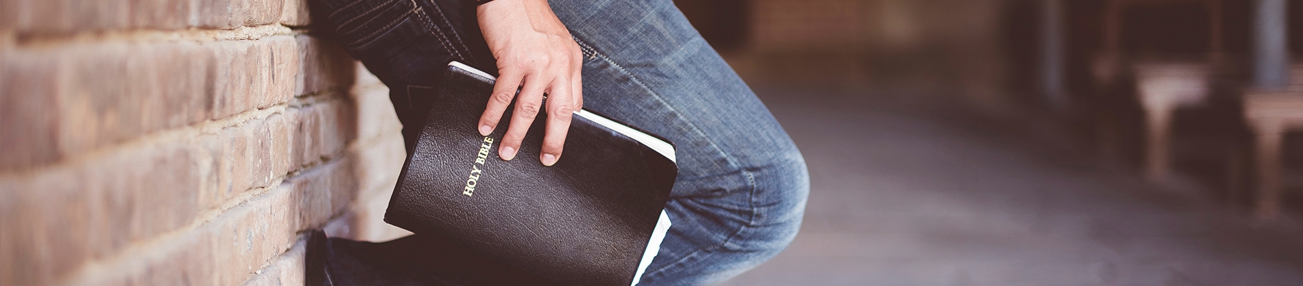 A man leaning against a brick wall holding a bible A man leaning against a brick wall holding a bible