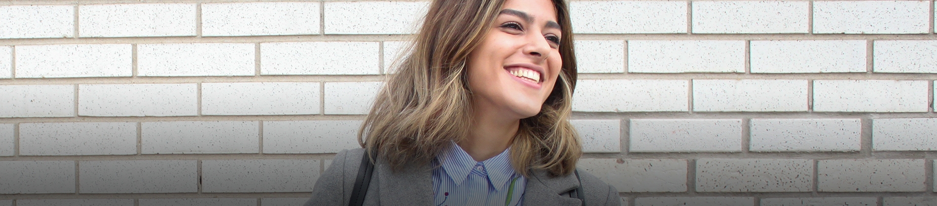 A women smiling with a brick wall behind her A women smiling with a brick wall behind her