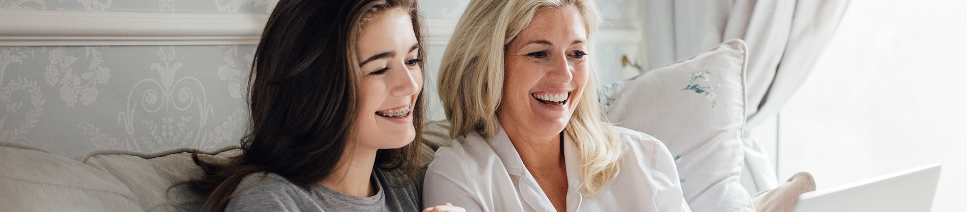 A smiling mother and teenage daughter sat on the sofa looking at a laptop A smiling mother and teenage daughter sat on the sofa looking at a laptop
