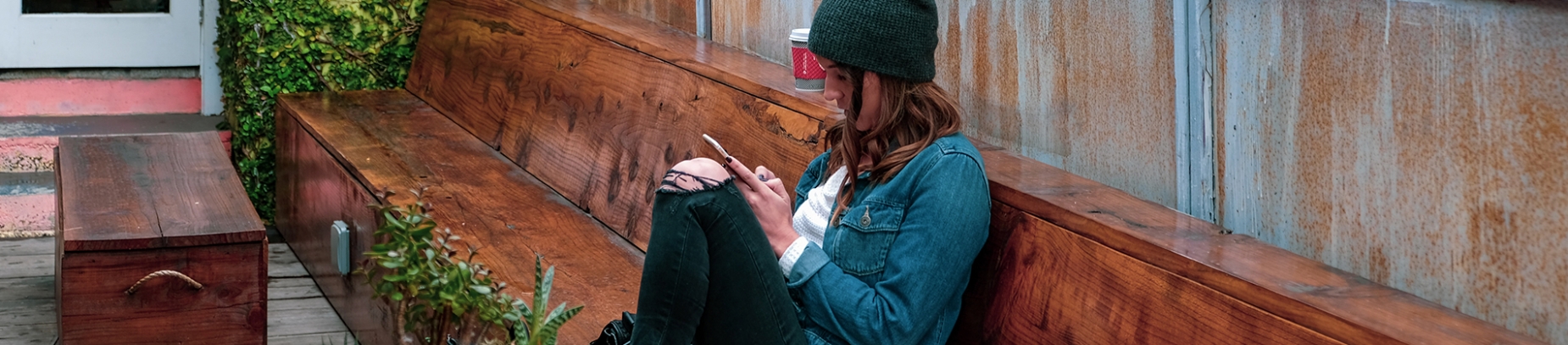A girl sat on a wooden seat looking at her phone A girl sat on a wooden seat looking at her phone