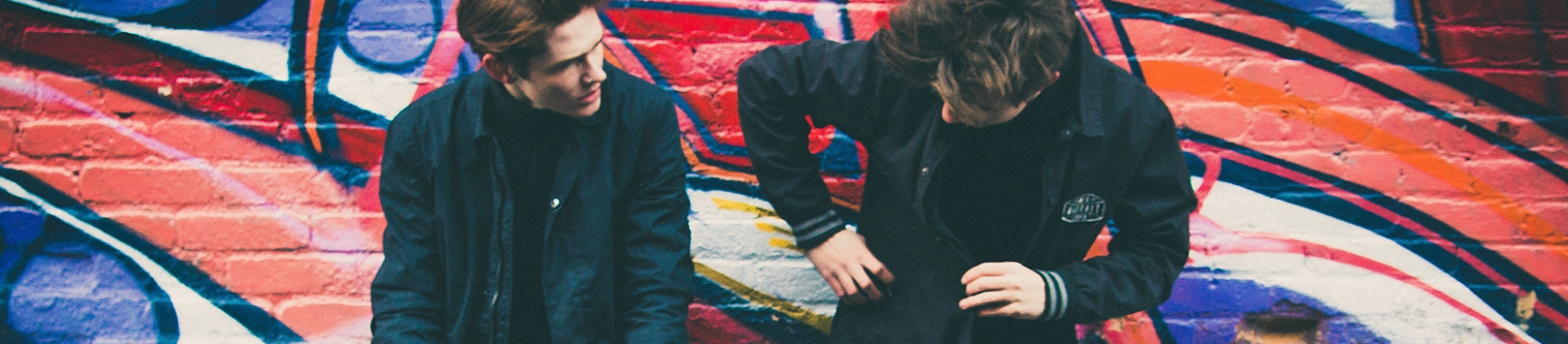 Two guys leaning against a colourful wall talking Two guys leaning against a colourful wall talking