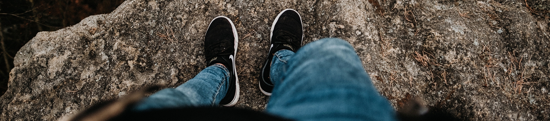 A man stood on the edge of a rock face looking down at his feet A man stood on the edge of a rock face looking down at his feet
