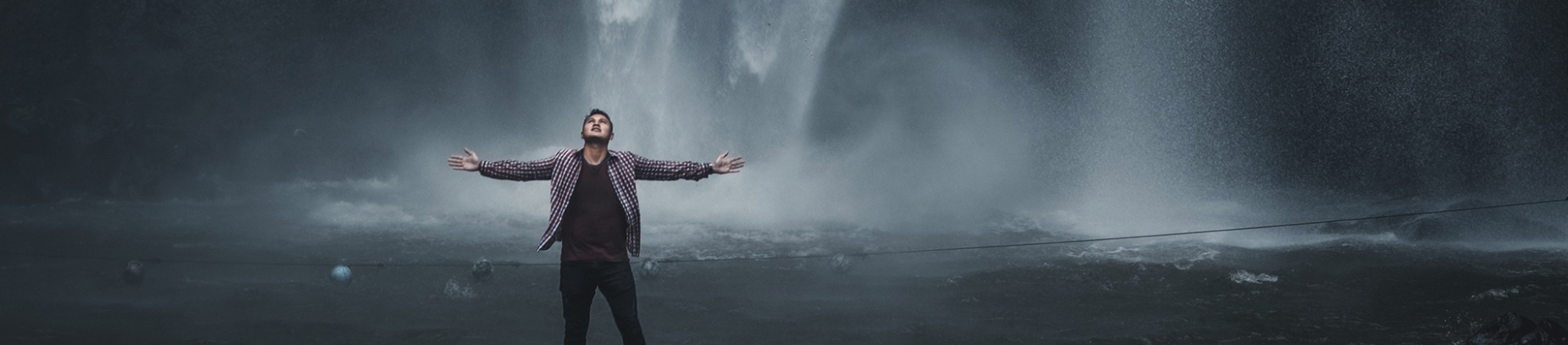 A man stood in front of a waterfall with his arms stretched out wide A man stood in front of a waterfall with his arms stretched out wide