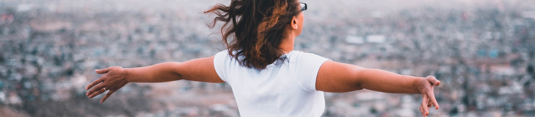 A women with her arms stretched out wide looking over a city A women with her arms stretched out wide looking over a city