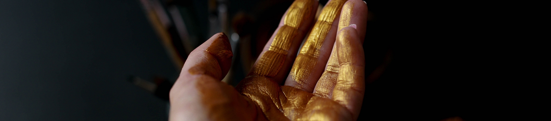 A persons hand with gold paint across the fingers A persons hand with gold paint across the fingers