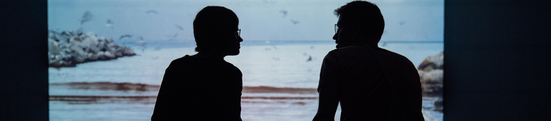 Two men sat talking to each other with the sea in front of them Two men sat talking to each other with the sea in front of them