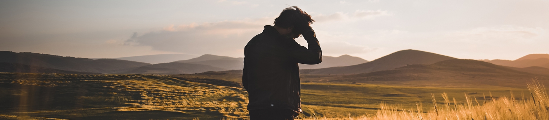 A man with his hand on his head looking out over a sunset and mountains A man with his hand on his head looking out over a sunset and mountains