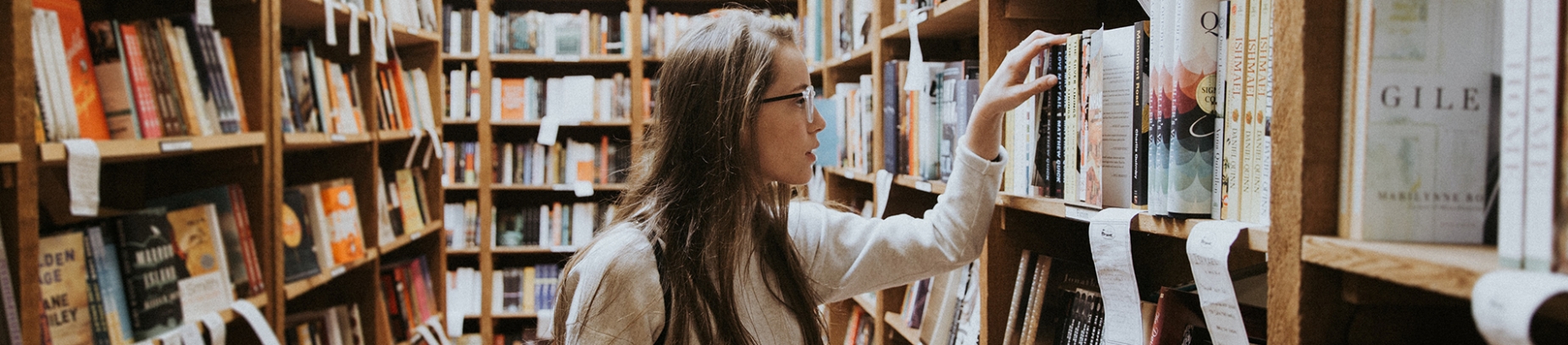A woman in a library looking through a book shelf A woman in a library looking through a book shelf