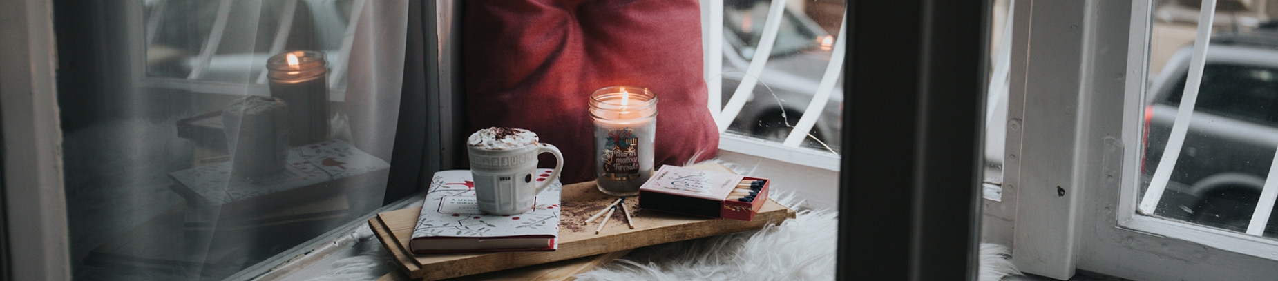 A cosy windowsill with a pillow, candle, hot chocolate and books A cosy windowsill with a pillow, candle, hot chocolate and books