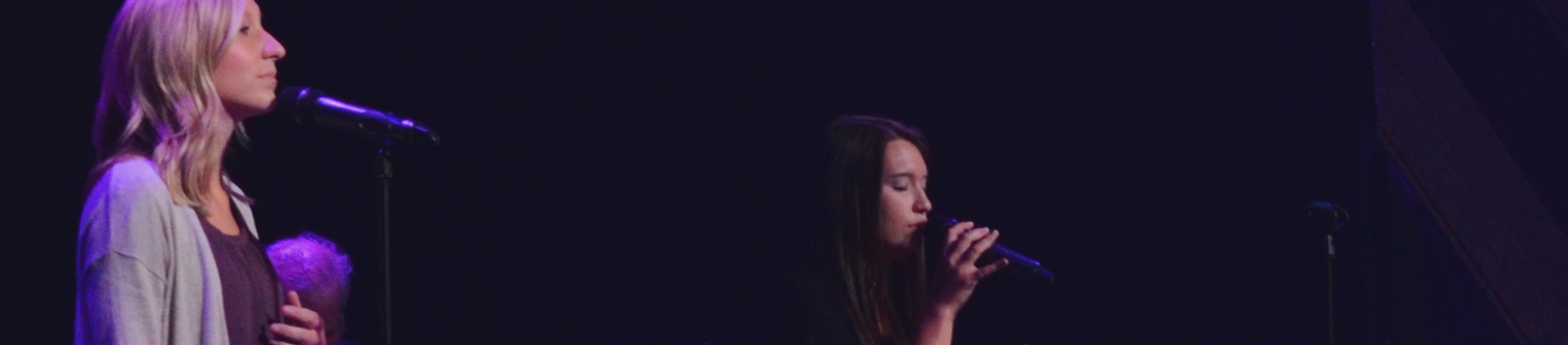Two women leading worship on a dark stage Two women leading worship on a dark stage