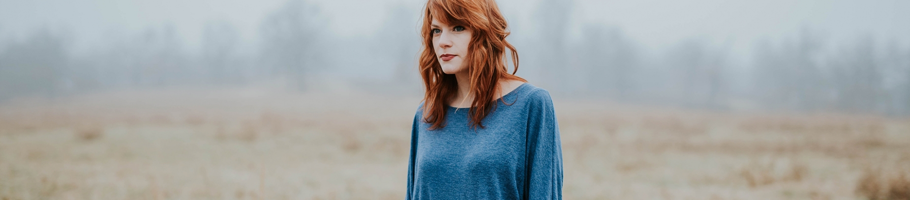 A women stood in a field looking longingly ahead A women stood in a field looking longingly ahead